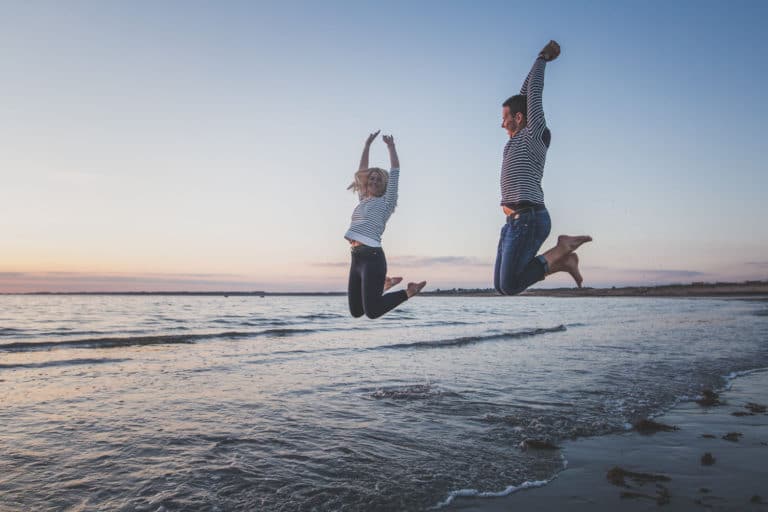 photo couple qui saute par dessus une vague en bord de mer lors d'une séance photo couple